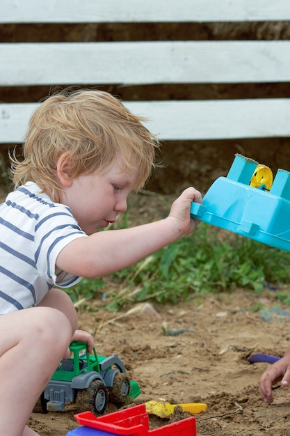 Kleine jongen speelt in het zand met plastic speelgoed. Kind speelt in de zandbak