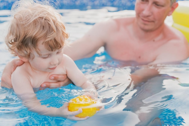 Kleine jongen speelt in het zwembad en leert zwemmen met zijn vader