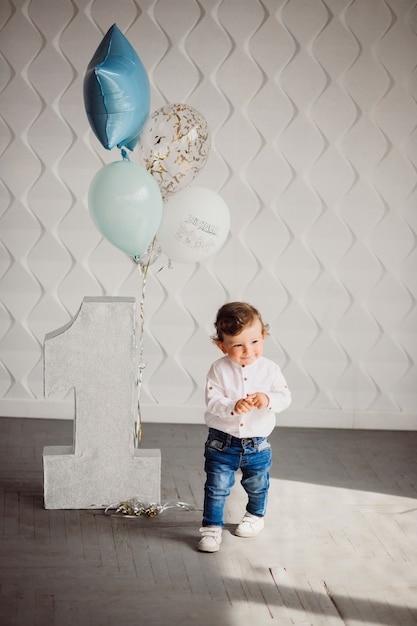 Kleine jongen speelt met blauwe ballonnen befoe grote nummer één in een gezellige kamer