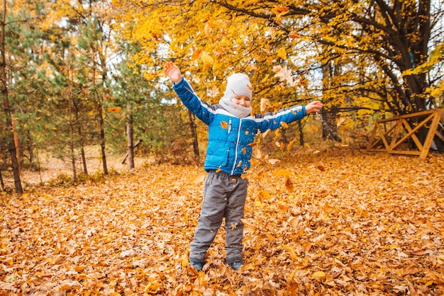 Kleine jongen speelt met gele bladeren in herfstpark