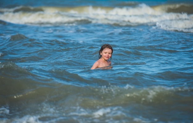 Kleine jongen speelt met golven op de blauwe zee Leuke jongen die plezier heeft op een zomervakantie in de zee