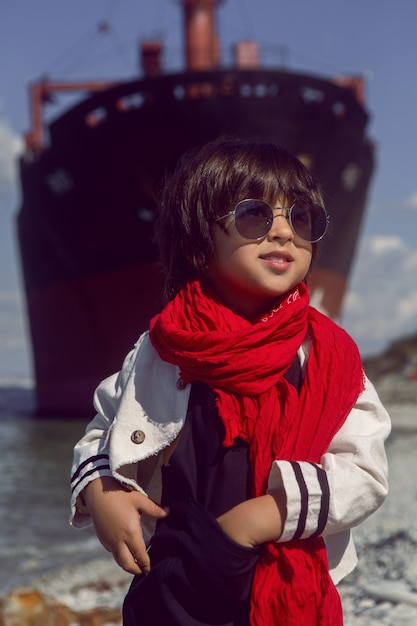 kleine jongen staan naast het schip aan kust