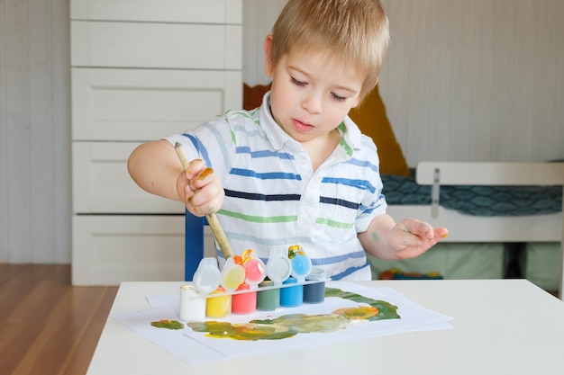 Kleine jongen tekent afbeelding op papier Kleuterkind in gestreepte kleding tekenen met verf