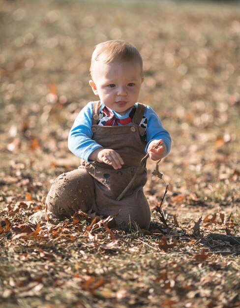 kleine jongen van 7 maanden oud zit op de herfstbladeren en loopt in de frisse lucht