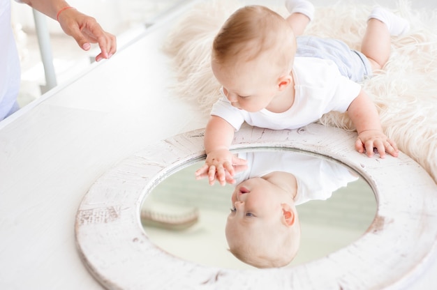 Kleine jongen van 7 maanden speelt op het witte tapijt in de slaapkamer met een spiegel