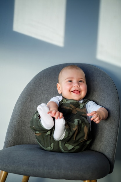 Kleine jongen van 8 maanden in overall, een wit overhemd en witte sokken zittend op een grijze stoel