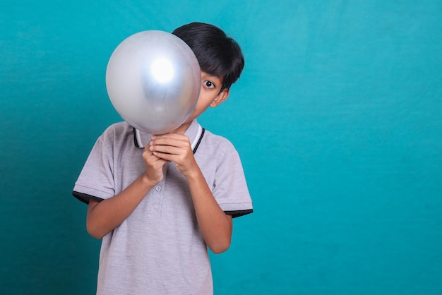 Kleine jongen verbergt zijn gezicht door grijze ballon geïsoleerd op groene achtergrond