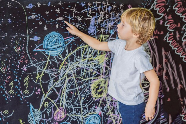 Kleine jongen wijst ruimteplaneten en sterren op de muur