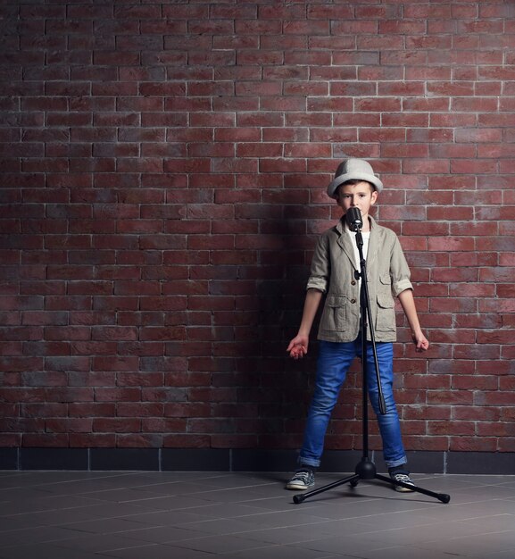 Kleine jongen zingen met microfoon op een bakstenen muur achtergrond