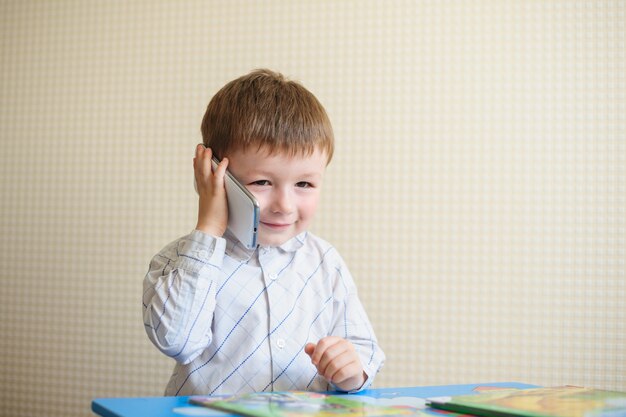 Kleine jongen zit aan bureau en praten over de telefoon