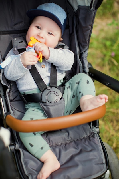 Kleine jongen zit in zijn grijze kinderwagen en speelt met speelgoed