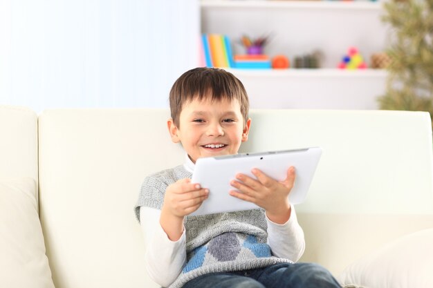Kleine jongen zittend op de bank met elektronische tablet