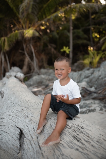 Kleine jongen zittend op een boomstam op een strand