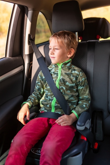 Kleine jongen zittend op een stoelverhoger vastgemaakt in de auto.