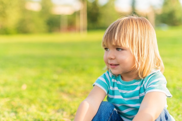 Kleine jongen zittend op gras in een park wegkijkend