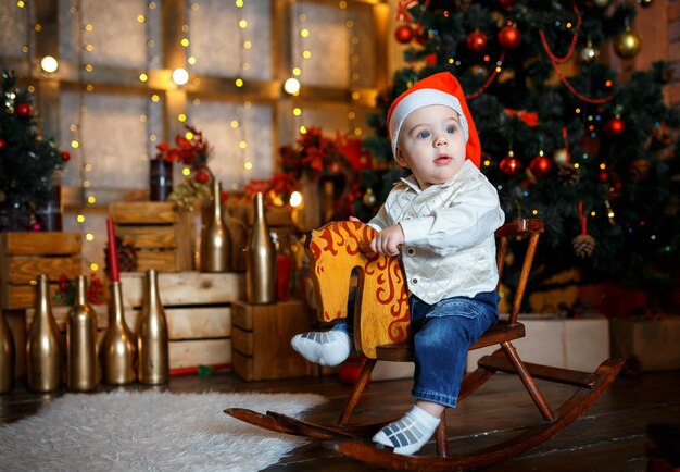 Kleine jongen zwaait op een paard bij de kerstboom