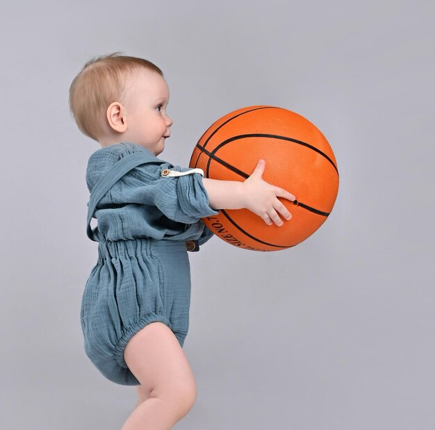 Kleine jongenspeuter houdt een grote oranje basketbal voor zich