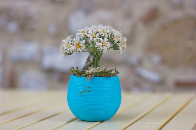 Kleine kamillebloemen in blauwe pot op de houten lijst