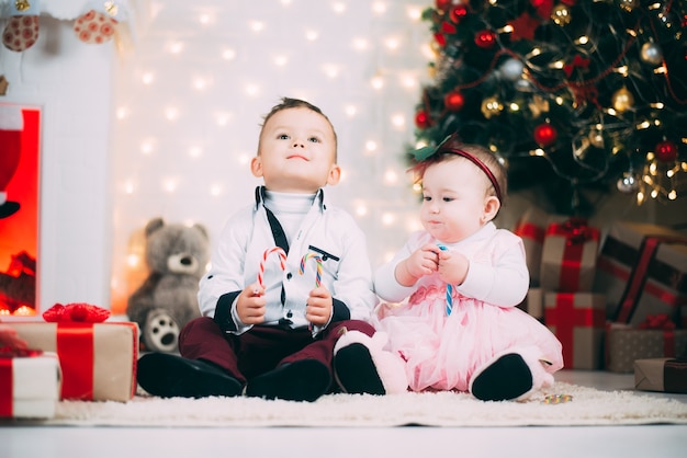 Kleine kinderen bij de kerstboom en de open haard met gekleurde snoepjes in hun handen