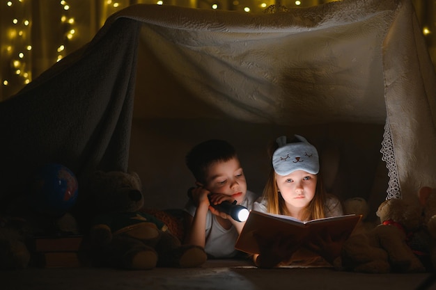 Kleine kinderen die een geweldig boek lezen Ze liggen in een leuke speelgoedtent in de speelkamer Jongen met zaklamp in de hand