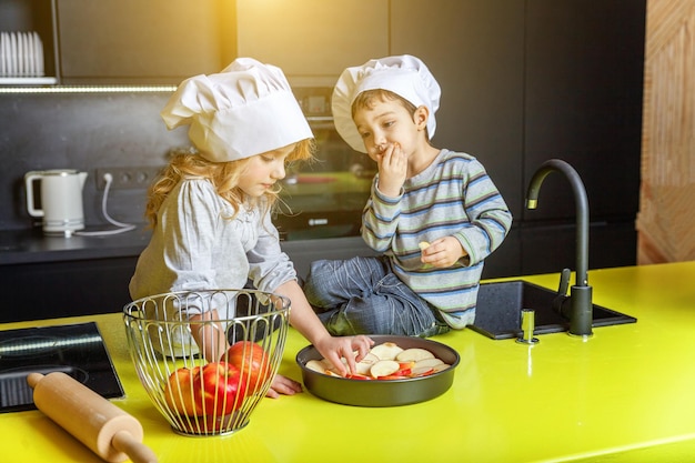 Kleine kinderen meisje en jongen met koksmuts bereiden zelfgemaakte appeltaart bakken in de keuken