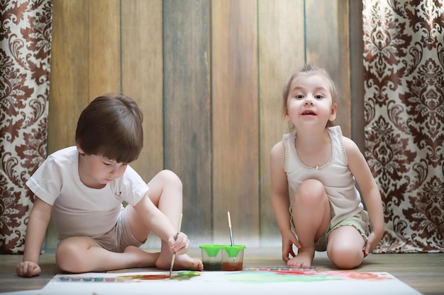 Kleine kinderen schilderen op een groot vel papier op de vloer