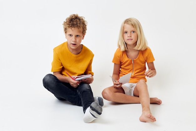 Foto kleine kinderen tekenen in notitieboekjes die op de vloer liggen, lichte achtergrond ongewijzigd