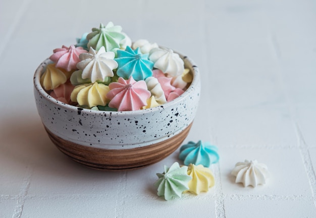 Kleine kleurrijke schuimgebakjes in de ceramische kom op tegelachtergrond