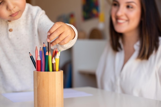 Kleine kleuter jongen tekenen met kleurpotloden met moeder of lerarenopleider. Focus op de potloden. Thuisonderwijs. Leergemeenschap. Montessorischool.