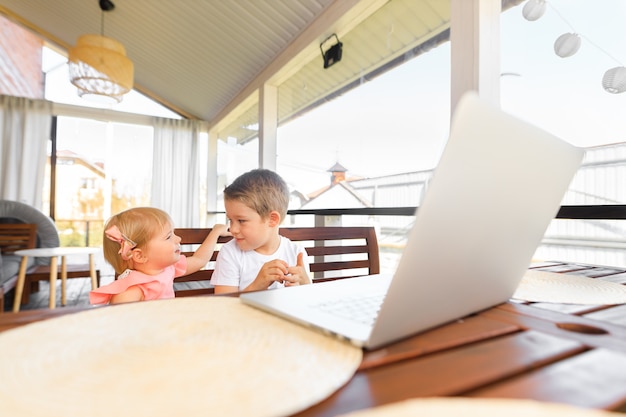 Foto kleine lachende kinderen broer en zus lachen en spelen laptop, communiceren videoconferentie chatten. ruim gezellig interieur.