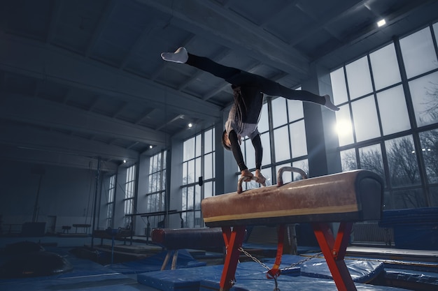 Kleine mannelijke turnster die traint in de sportschool, flexibel en actief. Kaukasische fit kleine jongen, atleet in sportkleding oefenen in oefeningen voor kracht, balans. Beweging, actie, beweging, dynamisch concept.