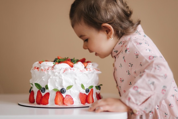 Kleine meid proeft voor het eerst verjaardagstaart Schattig klein meisje in een mooie jurk die cake met aardbeien proeft