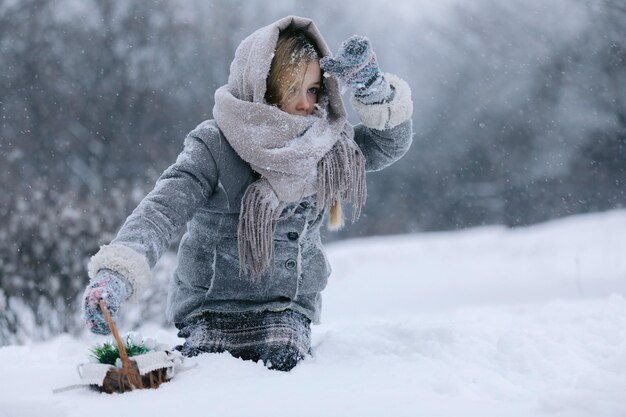 Foto kleine meisje met een mand gaat en zoekt de eerste bloemen onder de sneeuw in het bos in