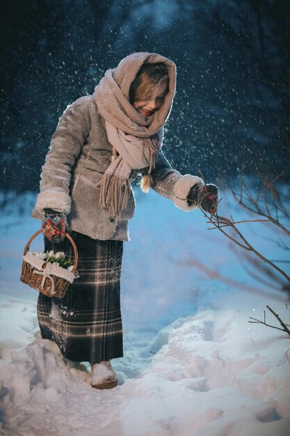 Kleine meisje met een mand gaat en zoekt de eerste bloemen onder de sneeuw in het bos in