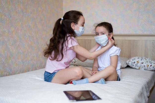 Kleine meisjes in beschermende maskers passen elkaars maskers thuis aan