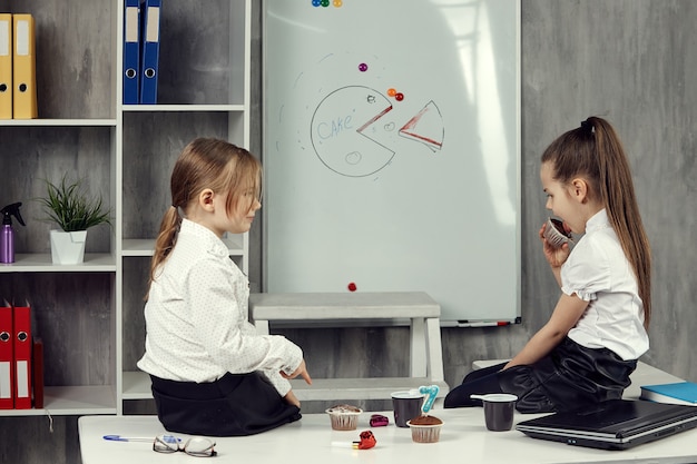 Kleine meisjes in de afbeeldingen van kantoormedewerkers zitten op een tafel en kletsen.