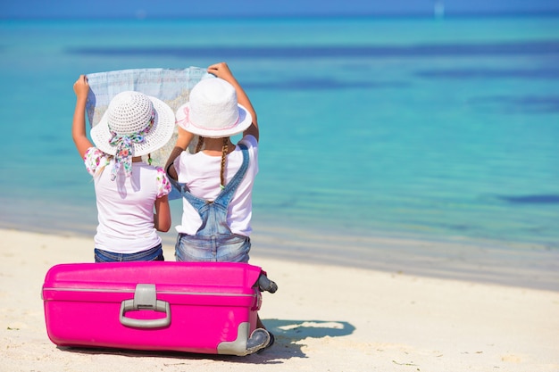 Kleine meisjes met grote koffer en kaart op tropisch strand