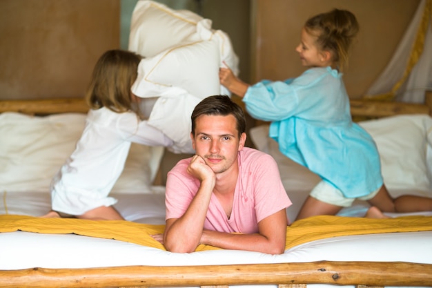 Kleine meisjes spelen thuis op bed in de buurt van hun vader