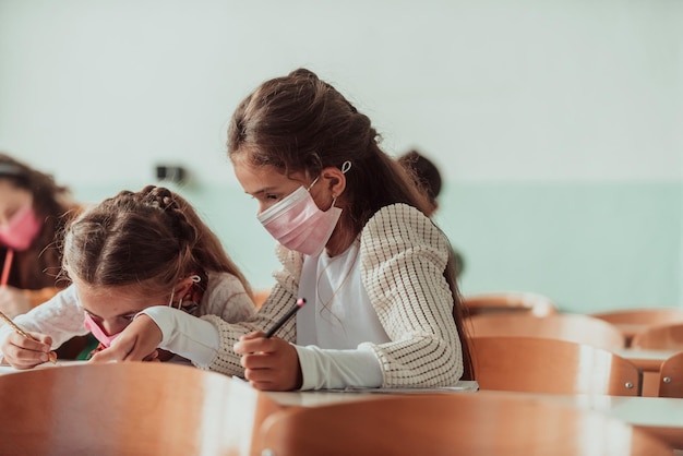 Kleine meisjes zitten aan schoolbanken terwijl ze een masker dragen tegen pandemische corona-virusbescherming Nieuw normaal onderwijs tijdens de Covid19-pandemie Selectieve focus Foto van hoge kwaliteit