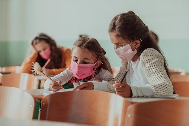 Kleine meisjes zitten aan schoolbanken terwijl ze een masker dragen tegen pandemische corona-virusbescherming Nieuw normaal onderwijs tijdens de Covid19-pandemie Selectieve focus Foto van hoge kwaliteit