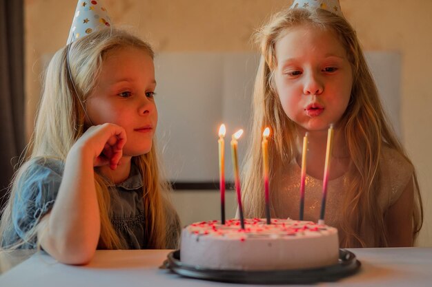 Kleine meisjes zussen tweeling blies vrolijk de kaarsjes uit op de verjaardagstaart thuis feestelijke pet verjaardag van het kind tijdens ziekte quarantaine isolatie