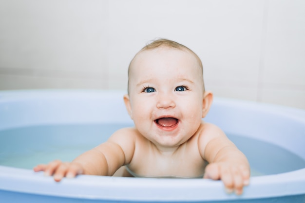 Kleine meisjesbaby baadt in de blauwe wastafel in de badkamer is erg leuk