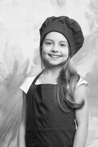 Kleine meisjeschef-kok met gelukkig gezicht in hoed en schort