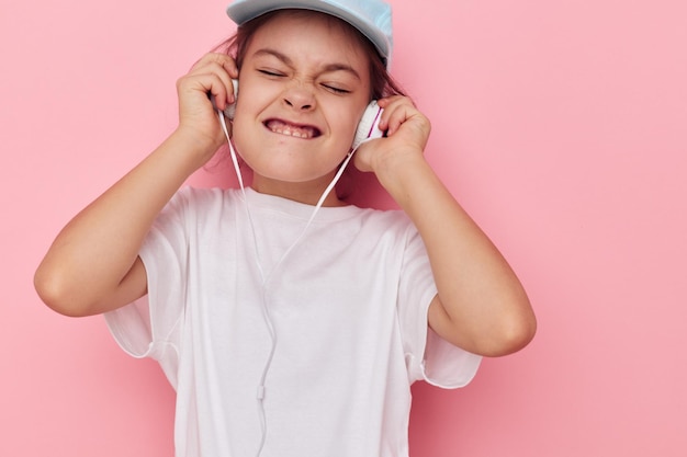 Kleine meisjeshoofdtelefoon in een wit t-shirt en een pet roze achtergrond