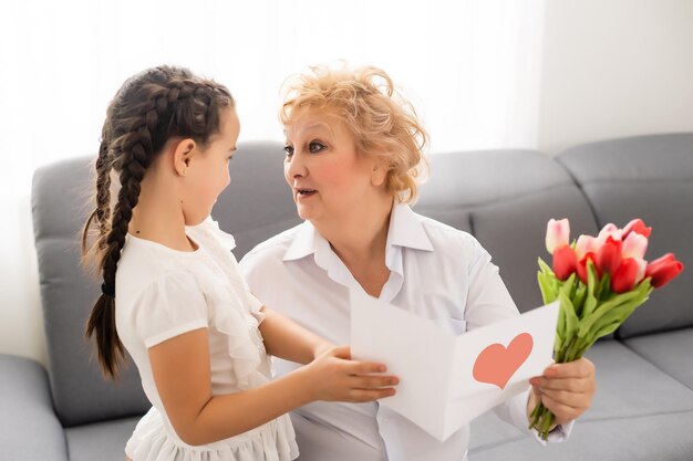 Kleine mooie kleindochter geeft haar grootmoeder een boeket roze tulpen. Het concept van familie, respect, generatie, moeder, opvoeding.