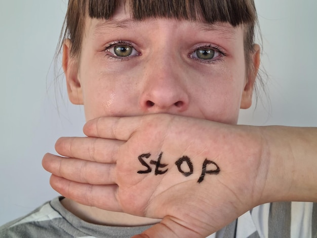 Foto kleine ontvoerde slachtoffer huilt naar de camera en houdt het woord stop in de handpalm kind