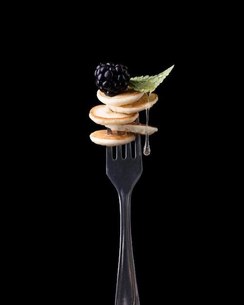 Kleine pannenkoek met bessen op een vork op een donkere achtergrond.
