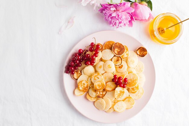 Kleine pannenkoeken met bessen, honing en bloemen op een wit tafellaken en ruimte voor tekst