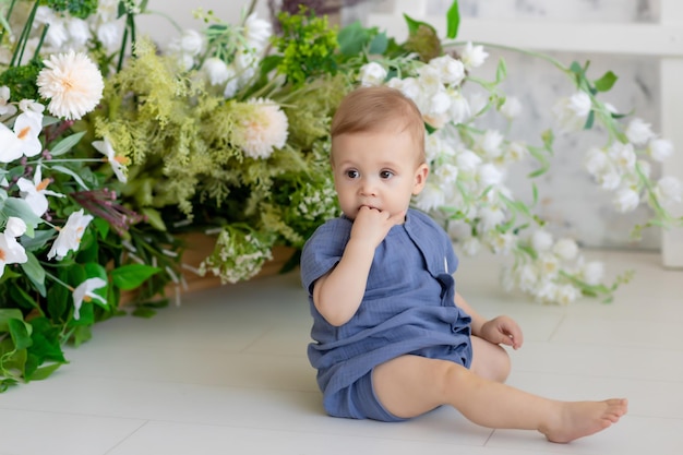 Kleine pasgeboren jongen in een blauw pak zit op de grond in de slaapkamer omringd door prachtige bloemen Babyproducten