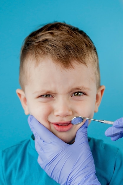 Kleine patiënt wil de mond van de tandarts niet openen op een blauwe achtergrond. Dantist behandelt tanden. close-up van tandarts behandeling van tanden van kleine jongen in het kantoor tandarts.